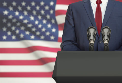 Politician making speech from behind a pulpit with national flag on background - United States
