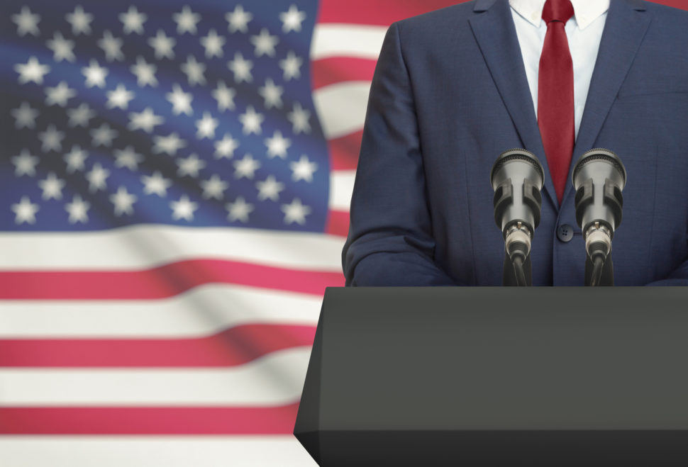 Politician making speech from behind a pulpit with national flag on background - United States